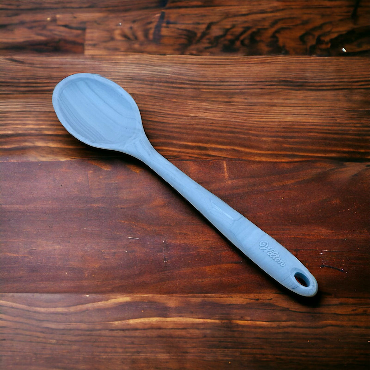 A blue silicone spoon with a long handle laid out on a wooden surface.
