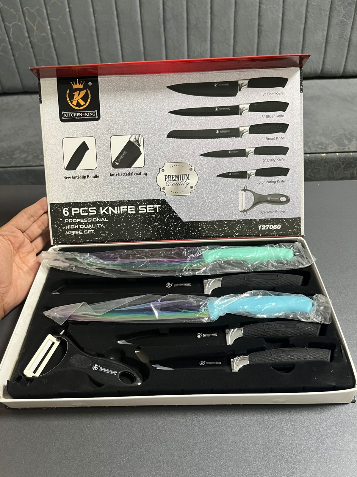 8-piece knife set in a box with a hand holding it, on a gray surface.